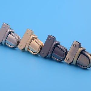 May include: Four metal clasps in different finishes: silver, gold, black, and bronze. Each clasp has a rectangular shape with a rounded edge and a decorative design.