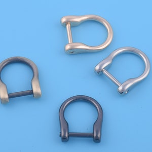 May include: Three metal D-rings in different finishes: gold, silver, and black. The rings are all the same size and shape, with a smooth, rounded finish.