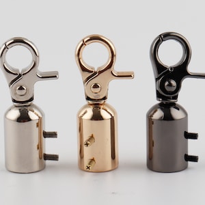 Könnte beinhalten: Drei Metall-Drehverschlüsse mit zylindrischer Basis und zwei Schrauben. Die Verschlüsse sind silber, gold und schwarz.