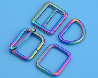 May include: Four iridescent metal hardware pieces: a rectangular slider, a D-ring, and two rectangular buckles. The hardware has a rainbow finish with hues of blue, green, yellow, and purple. The objects are on a light blue background.