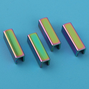 May include: Four iridescent metal U-shaped connectors. The connectors have a rectangular shape with a U-shaped opening. The colors shift from green to purple and gold. The connectors are on a light blue surface.