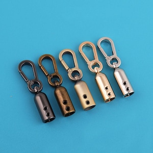 Könnte beinhalten: Fünf Metall-Drehhaken in verschiedenen Ausführungen: Schwarz, Bronze, Messing, Gold und Silber. Jeder Haken hat einen abgerundeten Zylinder mit zwei Löchern und einen federbelasteten Haken. Die Haken sind auf einem einfarbigen blauen Hintergrund angeordnet.