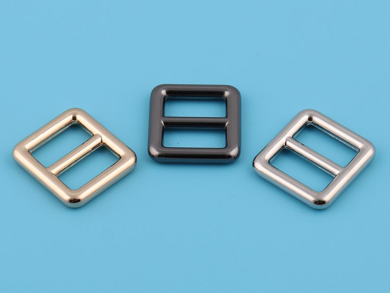 Pu&ograve; includere: Tre fibbie quadrate in metallo con una barra centrale. Le fibbie sono dorate, argentate e nere.