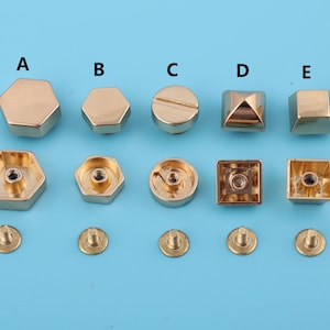 Peut inclure: Ensemble de cinq rivets et clous métalliques dorés de formes variées. On distingue des hexagones, un cercle avec une tête de vis, une pyramide et un carré. Les rivets sont présentés sur un fond bleu clair, pour la maroquinerie.