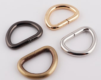 May include: Four metal D-rings in different finishes: gold, silver, black, and antique brass. These rings are commonly used for attaching straps, chains, or other accessories to bags, belts, or other items.