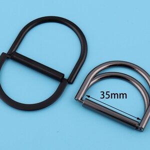 May include: Two black metal D-rings, one with a 35mm diameter, for attaching to bags, belts, or other accessories.