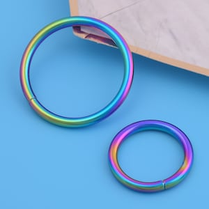 May include: Two iridescent metal rings, one larger than the other, on a blue background. The rings are smooth and have a rainbow finish.