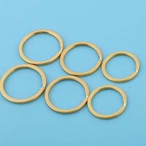 May include: Six gold-colored key rings of different sizes. The key rings are arranged in a semi-circle on a light blue background.