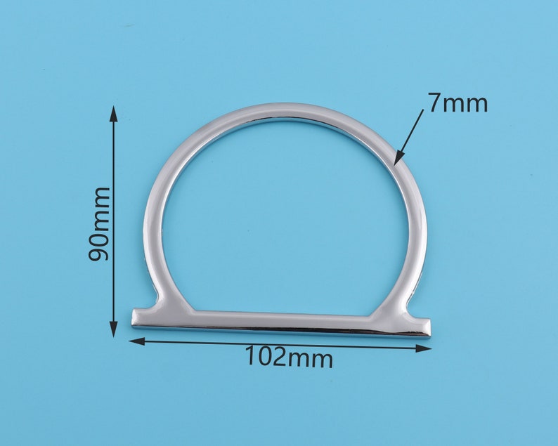 May include: Silver metal ring with a 7 mm width and a 102 mm diameter. The ring is a simple, circular shape with a flat, straight bar across the bottom.