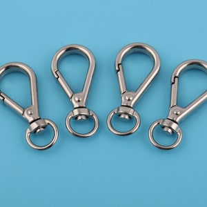 May include: Four silver swivel snap hooks with a rounded opening. The hooks are arranged in a row on a light blue background.