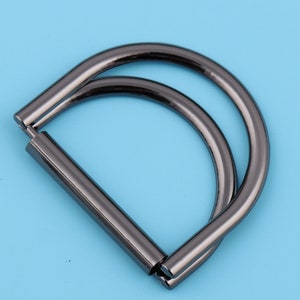 May include: A black metal D-ring with a double loop. The ring is designed for attaching to bags, purses, or other accessories.