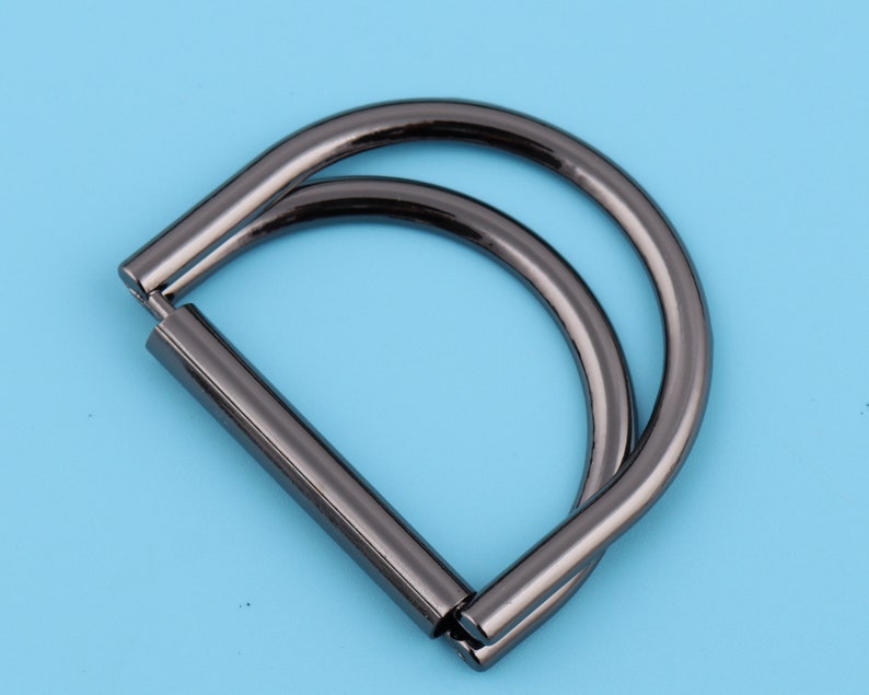 May include: A black metal D-ring with a double loop. The ring is designed for attaching to bags, purses, or other accessories.