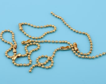 Puede incluir: Un collar de cadena de bolas doradas con múltiples cierres. La cadena está sobre un fondo azul claro.