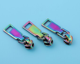 May include: Three iridescent zipper pulls in a rainbow color scheme. The pulls are made of metal and have a rectangular shape with a small hole at the top.