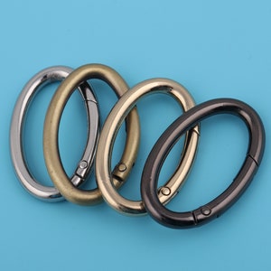 Puede incluir: Cuatro anillos metálicos ovalados en plata, oro y negro. Los anillos están todos cerrados y tienen un cierre giratorio.