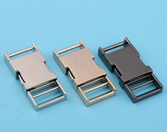Op de afbeelding: Drie metalen zij-ontgrendelingsgespen in zilver, goud en zwart.