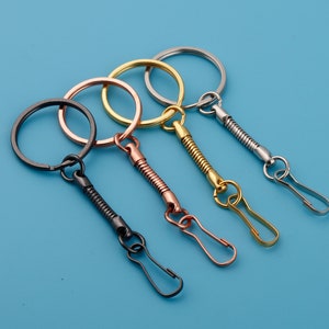 May include: Four keychains with different colored metal rings and swivel clips. The keychains are black, gold, silver, and rose gold.