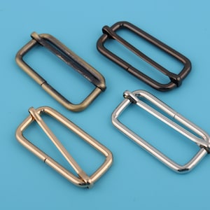 May include: Four metal slider buckles in different finishes: antique brass, gold, silver, and black. The buckles are rectangular with a single slider.