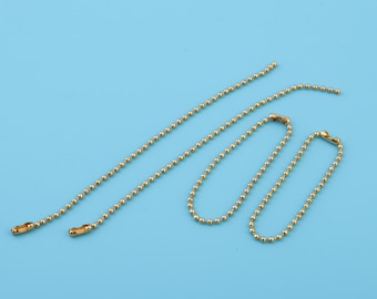 Puede incluir: Tres collares de cadena de bolas doradas con cierres. Las cadenas son de diferentes longitudes. Las cadenas están sobre un fondo azul claro.