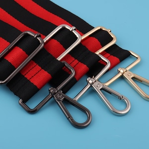 May include: Three metal clasps in gold, silver, and black. The clasps are attached to a red and black striped fabric strap.