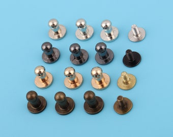 Könnte beinhalten: Sortiment an Metall-Druckknöpfen in verschiedenen Farben, darunter Gold, Silber und Schwarz. Die Knöpfe haben einen runden Kopf und eine flache Basis.