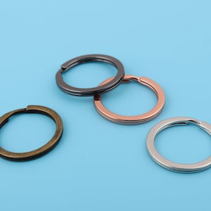 Könnte beinhalten: Drei Schlüsselringe in verschiedenen Ausführungen: Silber, Gold und Schwarz. Die Schlüsselringe sind alle gleich groß und gleich geformt.