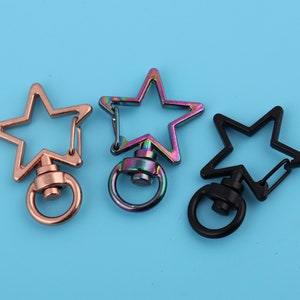 Puede incluir: Tres llaveros con forma de estrella en diferentes colores: oro rosa, iridiscente y negro. Cada llavero tiene un anillo de metal para sujetar las llaves.