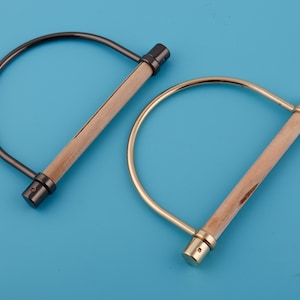 Puede incluir: Dos asas de metal en forma de D con inserciones de madera. El asa de la izquierda es negra y el asa de la derecha es dorada.