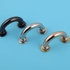May include: Three metal handles in black, silver, and gold finishes. Each handle is a rounded arch shape with a flat base.