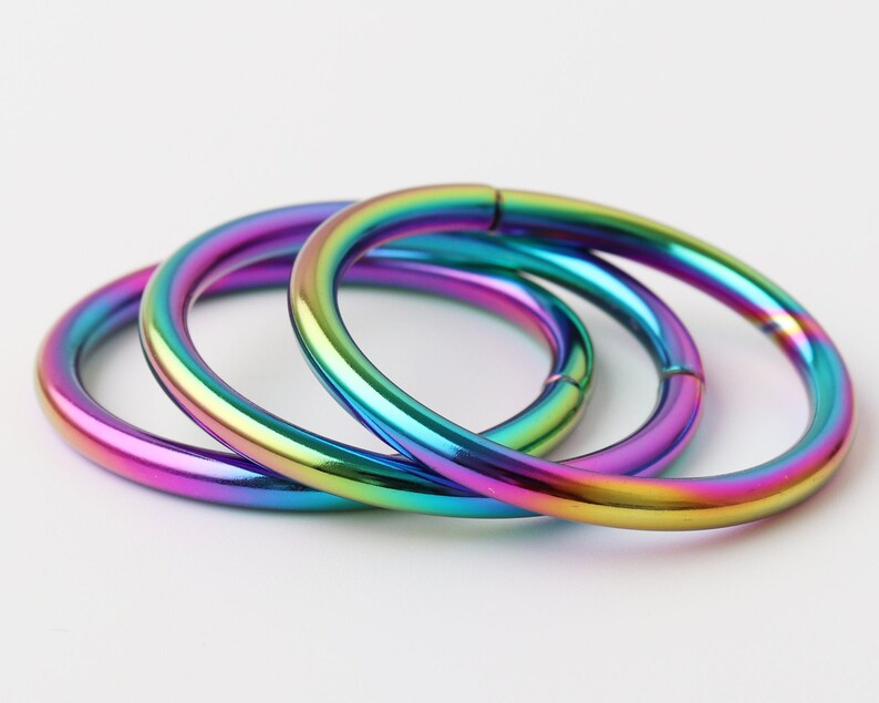 May include: Three iridescent metal rings, each with a different rainbow color pattern, are stacked on top of each other.