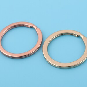 Peut inclure: Deux porte-clés, l'un en or et l'autre en or rose, sont présentés sur un fond bleu clair.