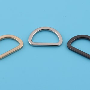 Puede incluir: Tres anillos en D de metal en diferentes acabados: dorado, plateado y negro. Los anillos son todos del mismo tamaño y forma.