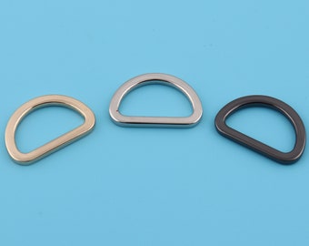 May include: Three metal D-rings in different finishes: gold, silver, and black. The rings are all the same size and shape.