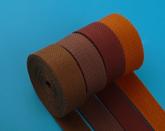 May include: A roll of woven fabric in shades of brown, burgundy, and orange against a blue background. The fabric appears to be a sturdy material, possibly canvas or webbing, suitable for various crafting or industrial uses.