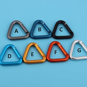 Può includere: Sette moschettoni triangolari in metallo di diversi colori: grigio, blu, nero, azzurro, oro, arancione e argento. Ogni moschettone è etichettato con una lettera: A, B, C, D, E, F e G.