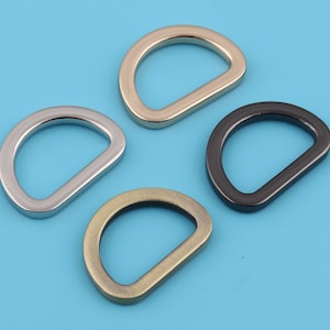 Puede incluir: Cuatro anillos en D de diferentes acabados: dorado, plateado, negro y latón antiguo. Estos anillos metálicos se utilizan comúnmente para sujetar correas, cadenas u otros herrajes a bolsos, cinturones u otros accesorios.
