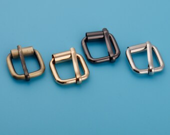 May include: Four metal belt buckles in different finishes: gold, brass, silver, and black. The buckles are all the same size and shape, with a square frame and a rectangular center.