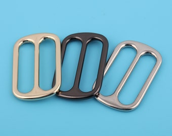 May include: Three metal slider buckles in gold, black, and silver. The buckles are rectangular with two oval-shaped openings.