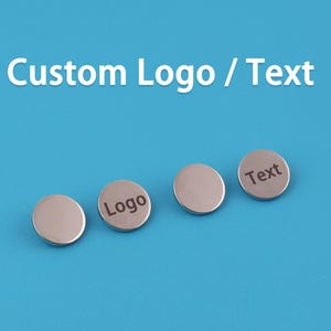 Op de afbeelding: Vier zilverkleurige, ronde, op maat gemaakte knopen met de woorden "Logo" en "Tekst" gegraveerd op twee ervan. De knopen liggen op een helderblauwe achtergrond. De tekst "Custom Logo / Text" staat bovenaan.