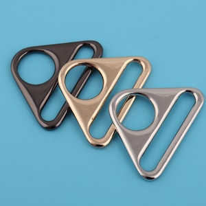 Op de afbeelding: Drie driehoekige metalen schuifgespen in zwart, goud en zilver.