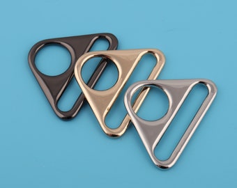 Puede incluir: Tres hebillas deslizantes de metal de forma triangular en negro, dorado y plateado.