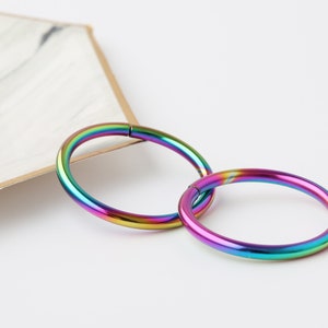 May include: Two rainbow colored metal hoop earrings. The hoops are seamless and have a polished finish.