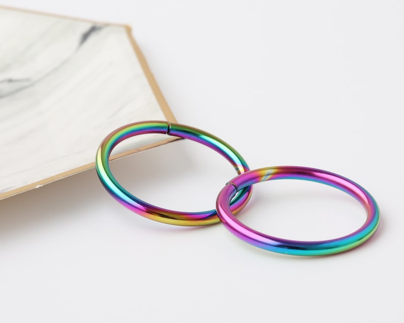 May include: Two rainbow colored metal hoop earrings. The hoops are seamless and have a polished finish.