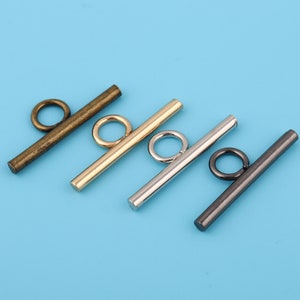 May include: Four toggle clasps in different finishes: antique brass, gold, silver, and black. Each clasp has a straight bar with a round loop at each end.