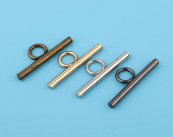 May include: Four toggle clasps in different finishes: antique brass, gold, silver, and black. Each clasp has a straight bar with a round loop at each end.