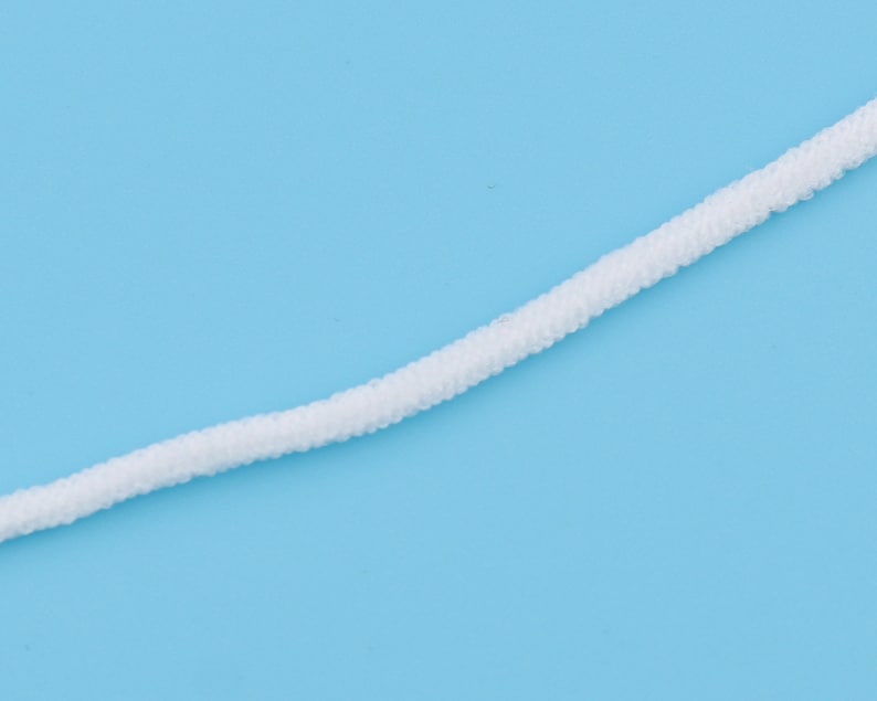 Op de afbeelding: Wit elastisch koord, vaak gebruikt voor gezichtsmaskers, tegen een lichtblauwe achtergrond.