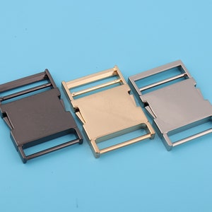 May include: Three metal clasps in black, gold, and silver. The clasps are rectangular with a smooth finish and a single bar across the center.