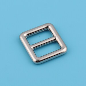 Pu&ograve; includere: Fibbia in metallo argentato di forma quadrata con due aperture rettangolari.