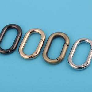 Puede incluir: Cuatro cierres metálicos ovalados en diferentes acabados: negro, dorado, bronce y plateado. Los cierres están abiertos y listos para ser unidos a una bolsa, bolso u otro artículo.