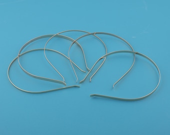 Può includere: Diverse fasce per capelli in metallo color argento sono disposte su uno sfondo blu uniforme. Le fasce hanno un design semplice e curvo, con una fascia piatta sulla parte superiore e lati sottili e dritti.